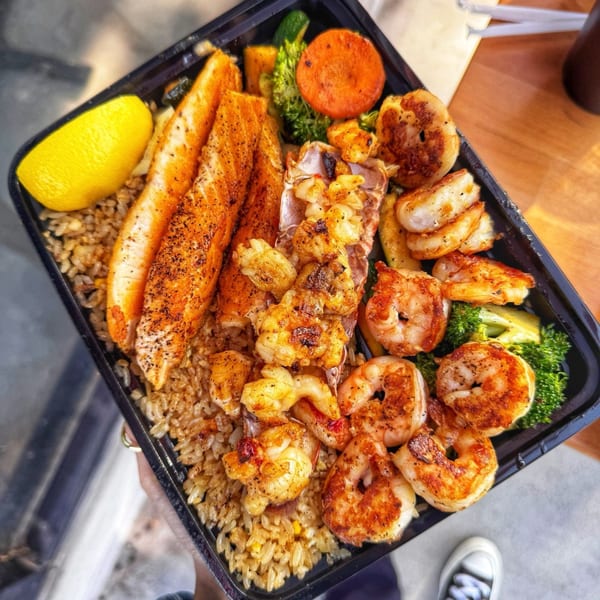 Habachihana Grill's salmon, shrimp, and lobster with fried rice, vegetables, and a lemon wedge.