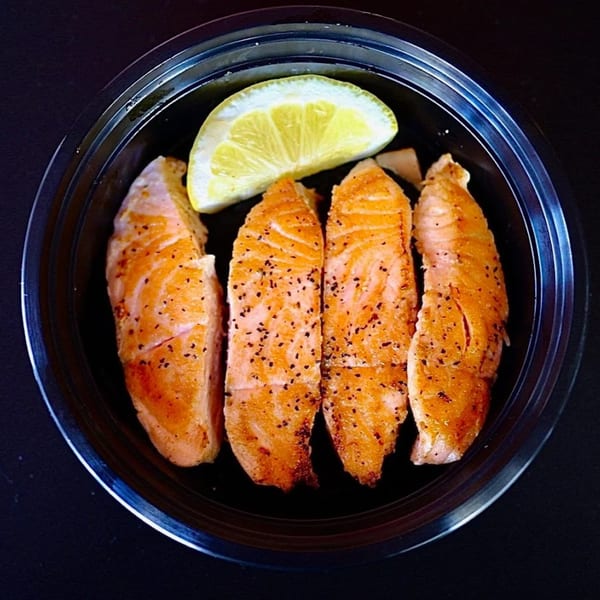 Four seasoned salmon fillets and a lemon wedge in a black bowl.
