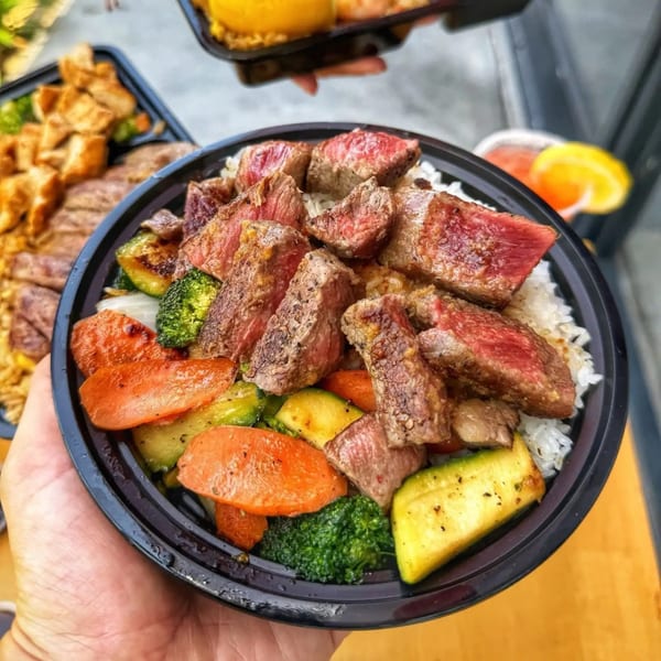A hand holds a Habachihana Grill bowl filled with steak, rice, and mixed vegetables.